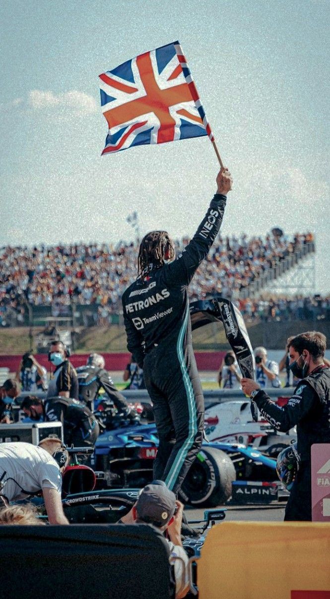 a man holding up a flag in front of a large crowd at a race track