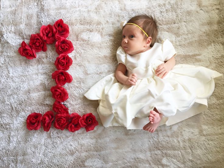 a baby in a white dress is laying next to the word love spelled out with red roses