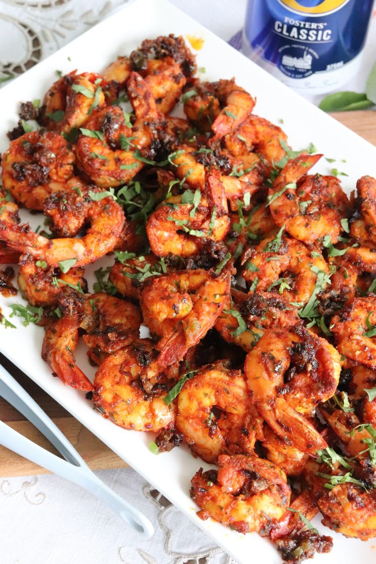 a white plate topped with cooked shrimp and garnished with herbs next to silverware