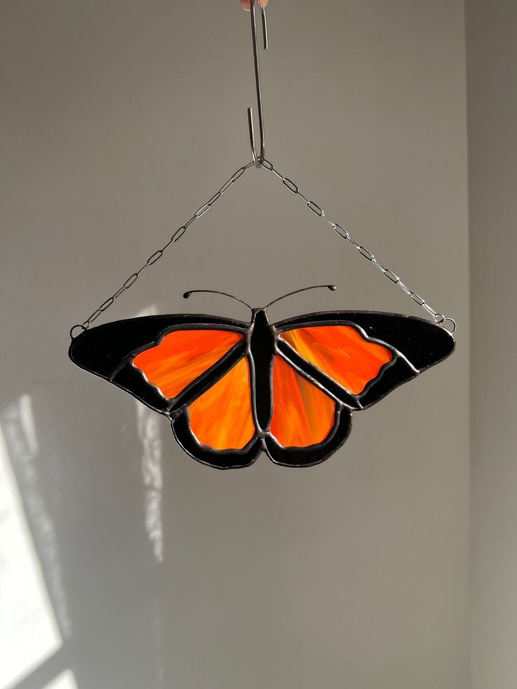 an orange and black butterfly hanging from a metal hook in a room with sunlight coming through the window