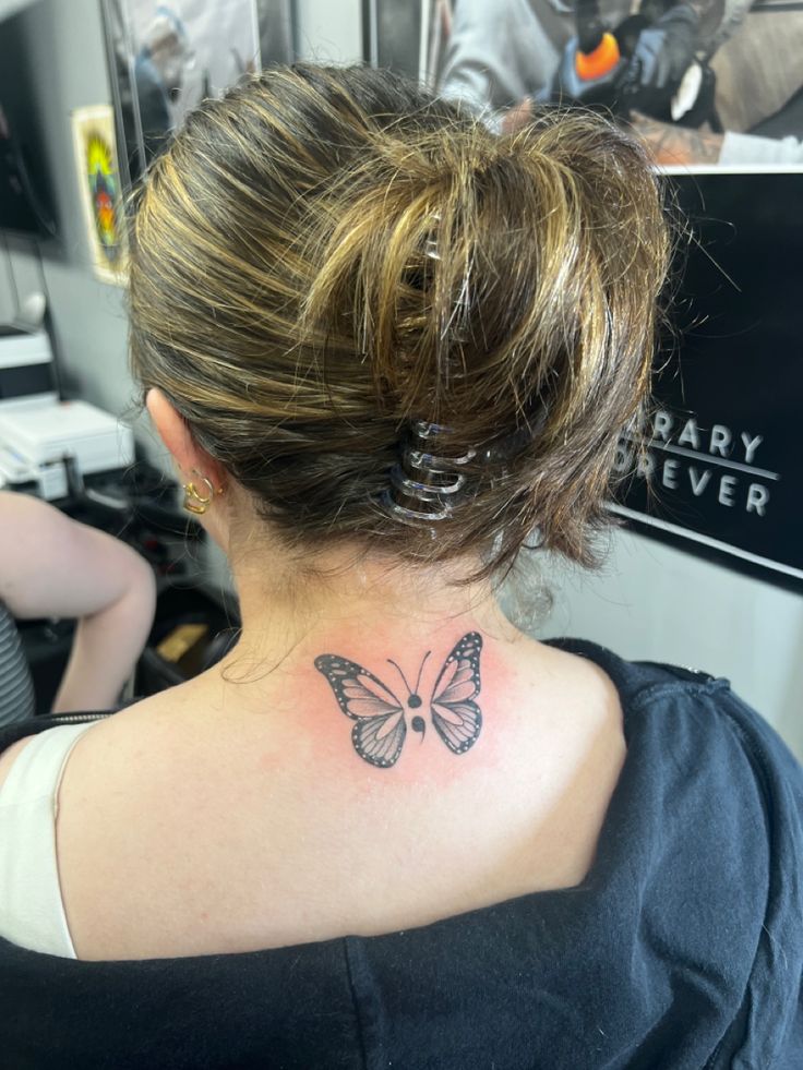 a woman with a butterfly tattoo on her back neck and behind her ear, looking at the camera