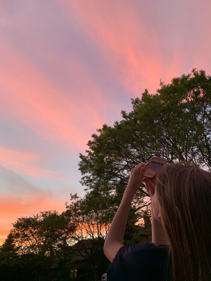 a girl is looking up into the sky with her camera in hand at sunset or dawn