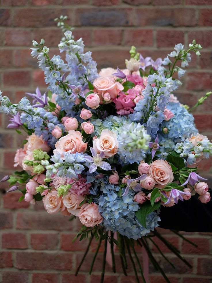 a bouquet of pink and blue flowers in front of a brick wall