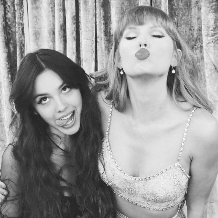 two beautiful women standing next to each other in front of a curtain covered wall with curtains behind them