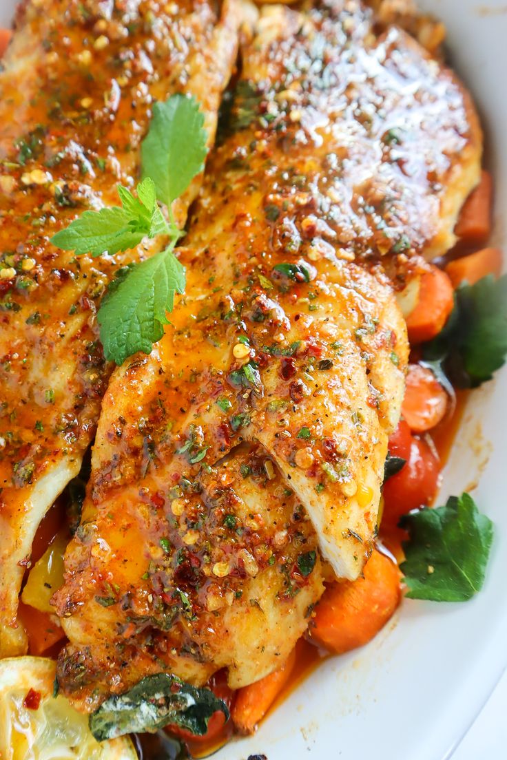 a white plate topped with chicken, carrots and potatoes covered in seasoning next to parsley