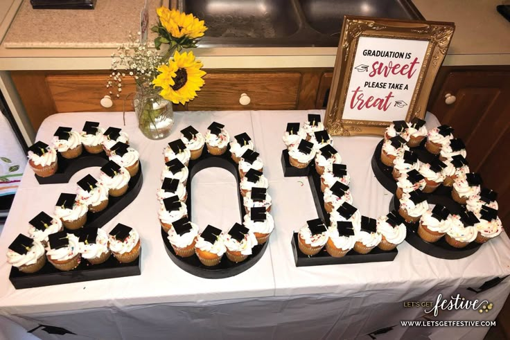 a table topped with cupcakes covered in frosting next to a framed sign