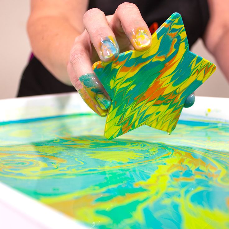 a woman is holding a piece of paper in her hand and painting on the table