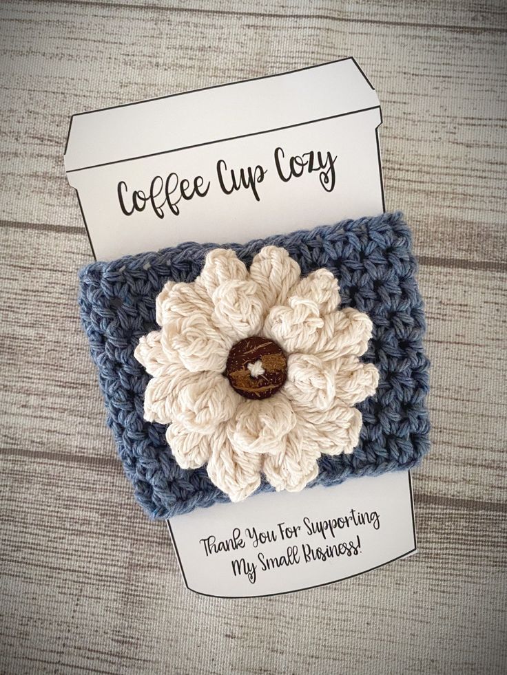 a crocheted coffee cup cozy with a white flower on the front and brown center