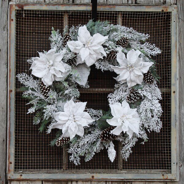 a wreath with white poinsettis and pine cones is hung on an old window