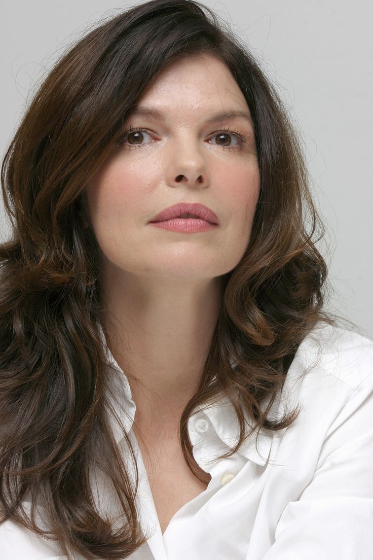 a woman with long brown hair wearing a white shirt and looking off to the side