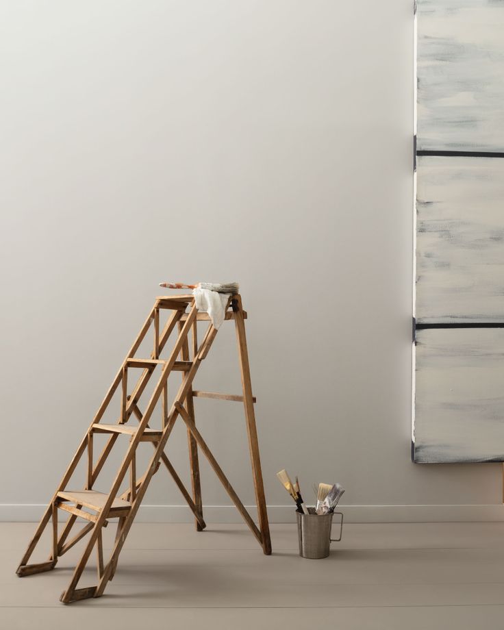 a ladder leaning against a wall next to a bucket and paintbrush on the floor