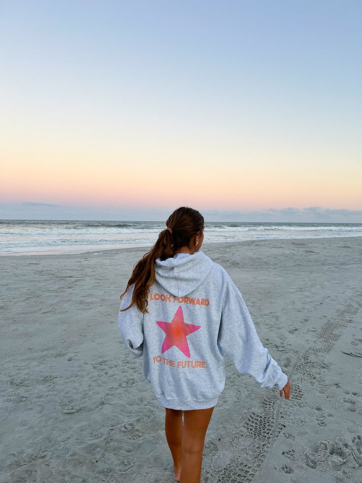 a woman walking on the beach with her back to the camera, wearing a hoodie