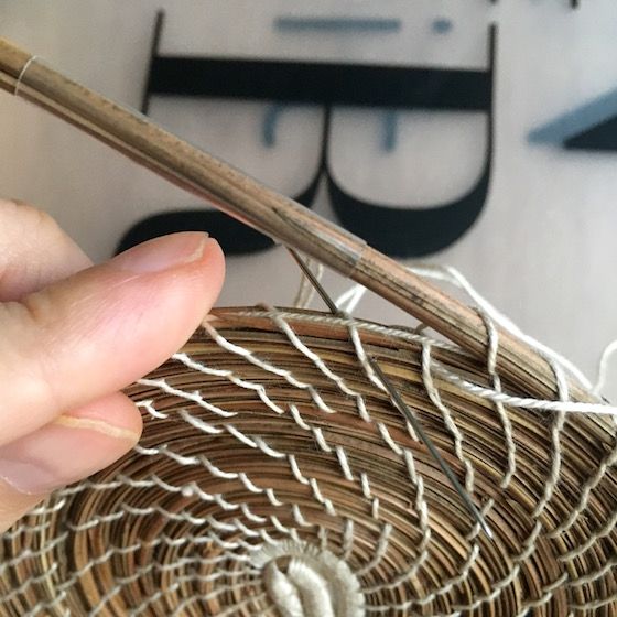 a person holding a pair of chopsticks over a basket with yarn on it