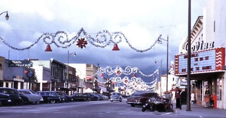 an empty street with cars parked on both sides and christmas lights strung from the buildings