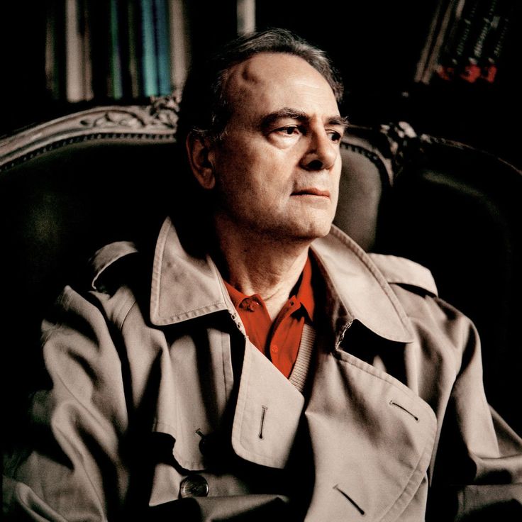 a man sitting in a chair wearing a trench coat and looking off into the distance