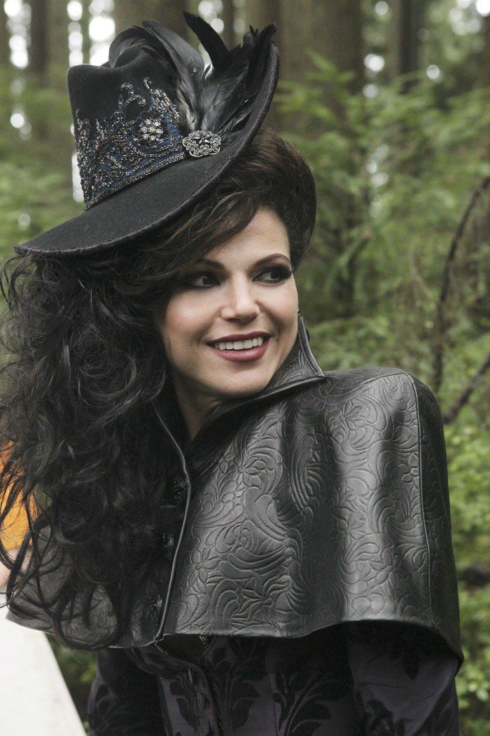 a woman with long hair wearing a black hat and cape on her head, smiling at the camera