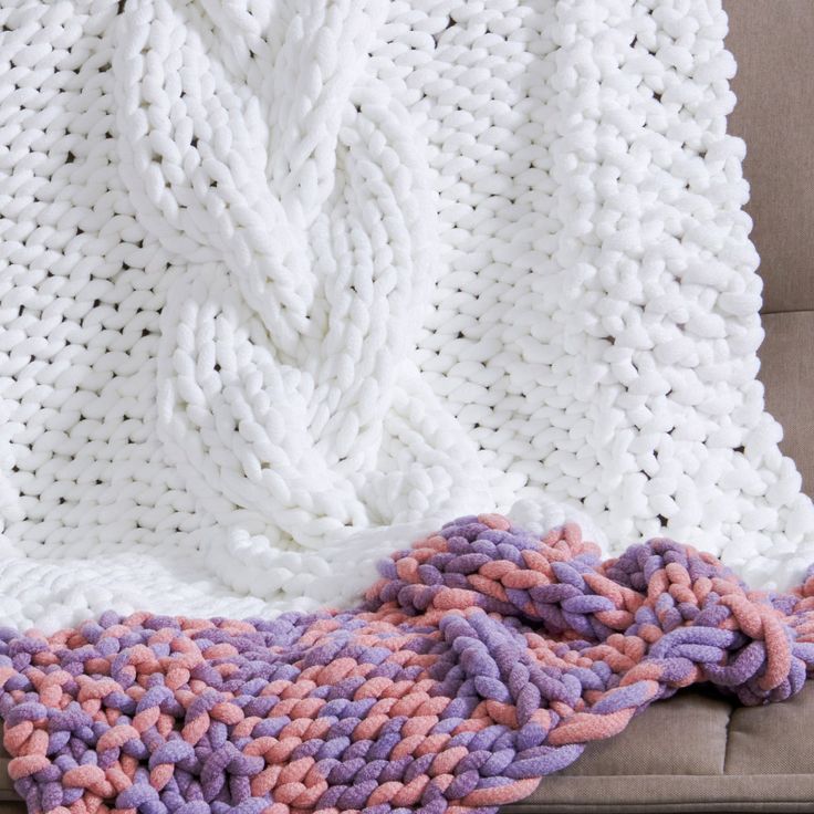 a white and pink knitted blanket sitting on top of a couch next to a pillow