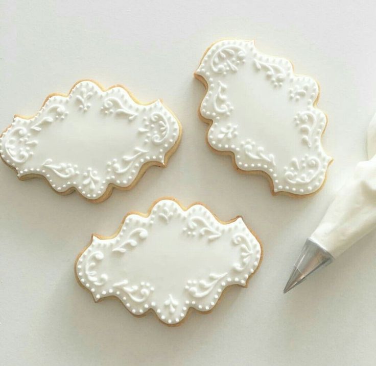 three decorated cookies and a pen on a white tablecloth with the edge cut out