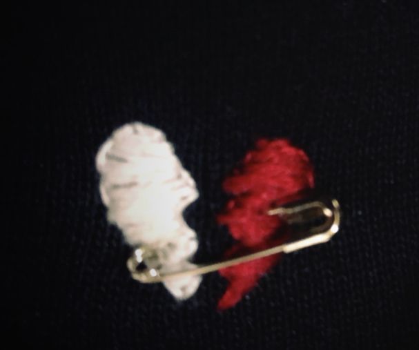 a red and white piece of yarn sitting on top of a black cloth next to a metal pin