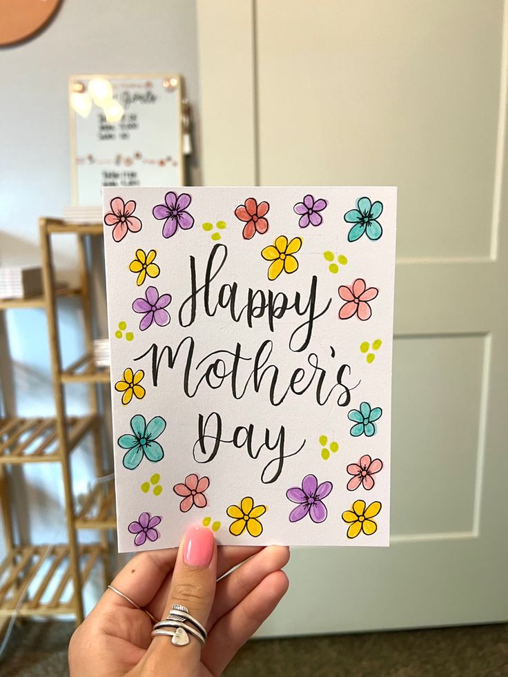 a woman holding up a card that says happy mother's day with flowers on it