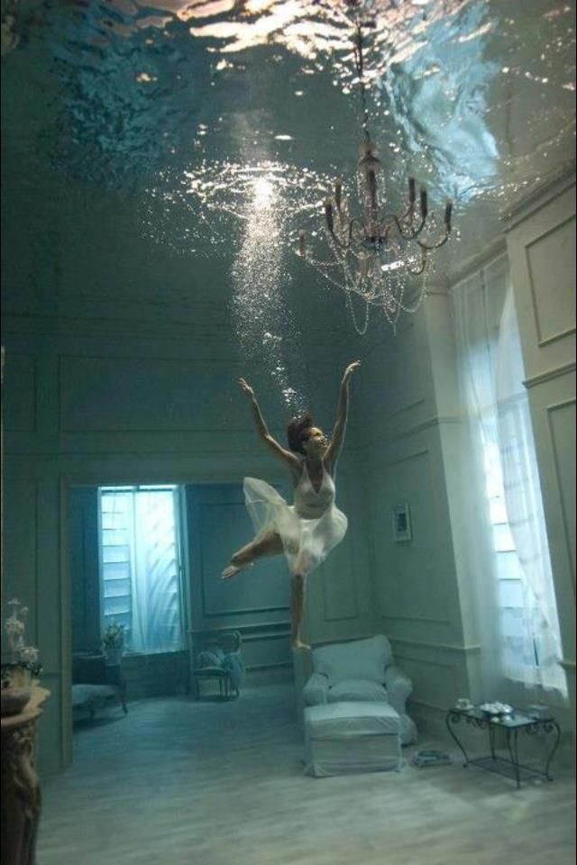 a woman in white dress under water with chandelier hanging from ceiling above her