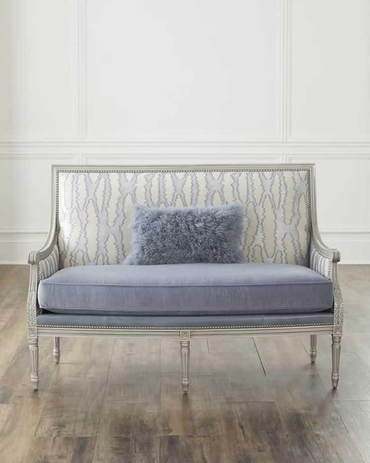 a couch with a blue pillow on it in front of a white wall and wooden floor