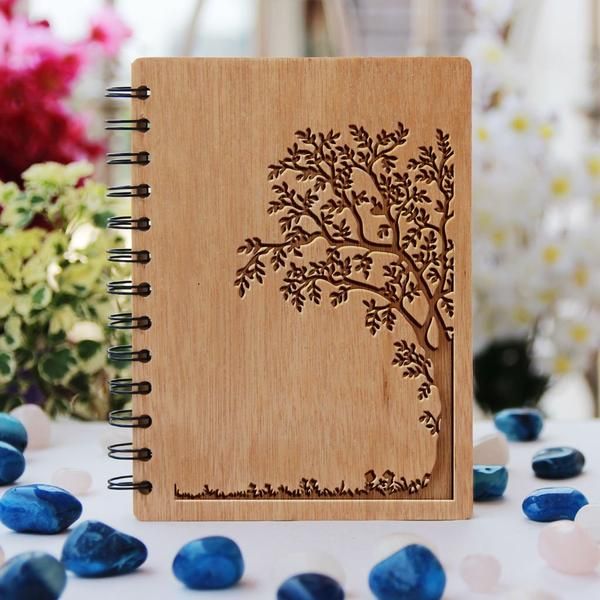 a wooden notebook with a tree carved on the cover and blue stones scattered around it