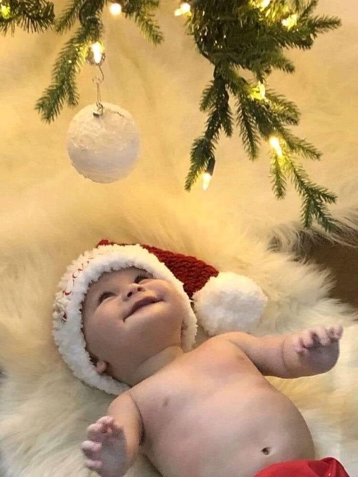 a baby wearing a santa hat laying under a christmas tree