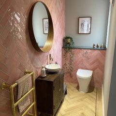 a bathroom with pink tiles and gold fixtures, including a round mirror above the sink