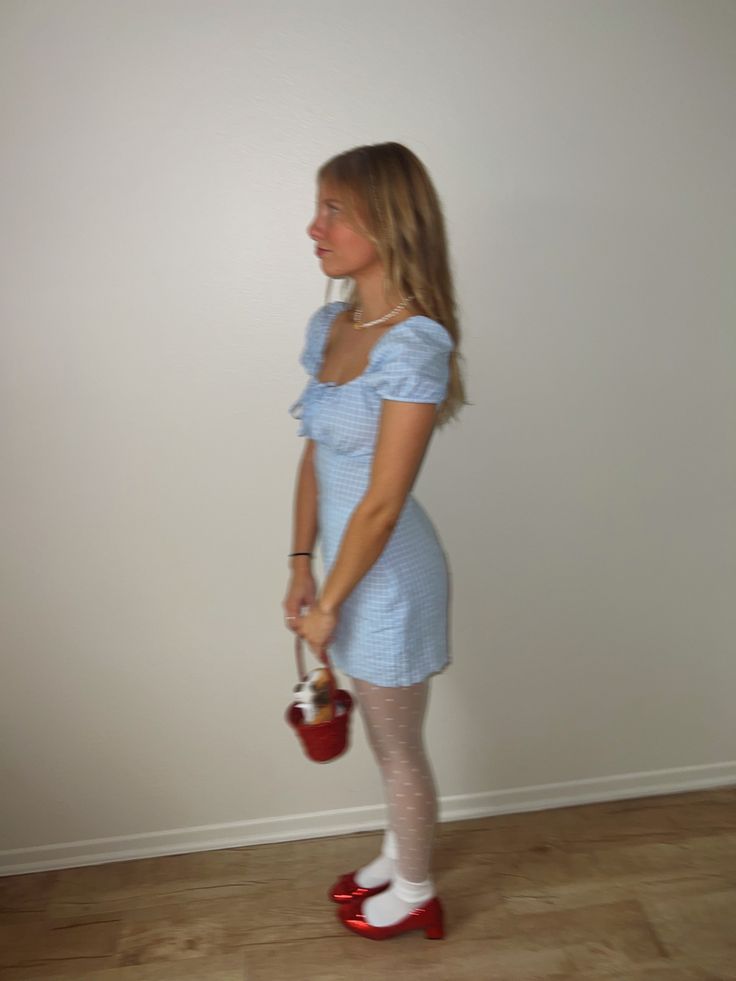 a woman in a blue dress is holding a red purse and wearing white tights