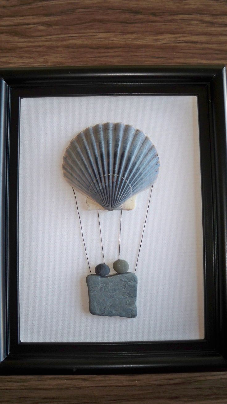 an art piece with a shell and two rocks in it hanging on the wall next to a black frame