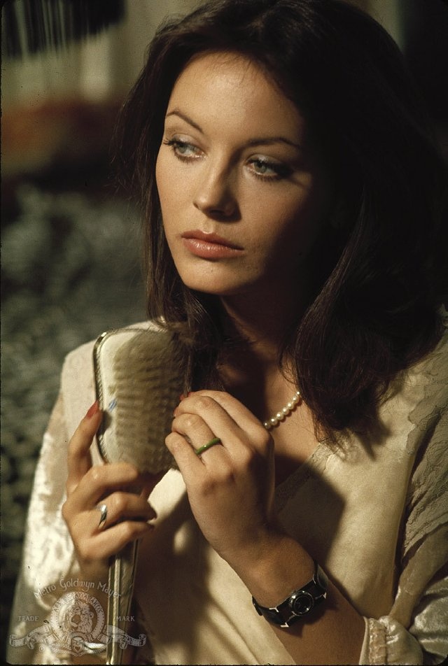 a woman is holding a hair brush and looking at the camera while wearing pearls on her necklace