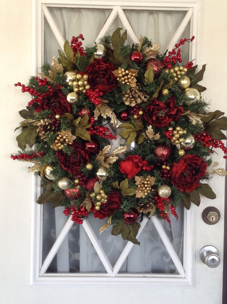 a wreath on the front door decorated with red flowers and greenery