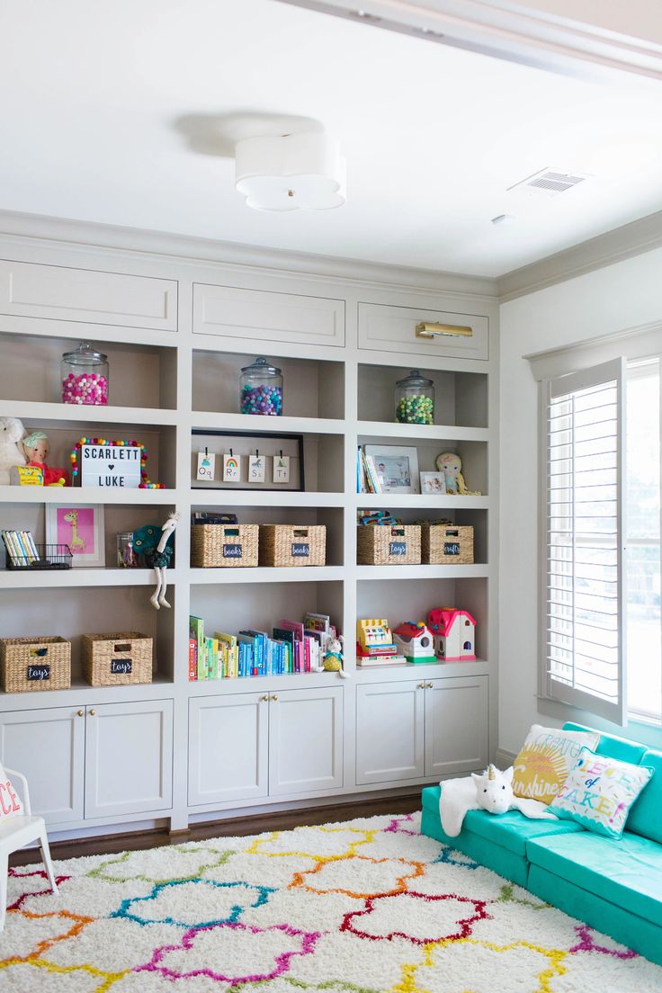 a living room filled with lots of white bookshelves and colorful rug on the floor