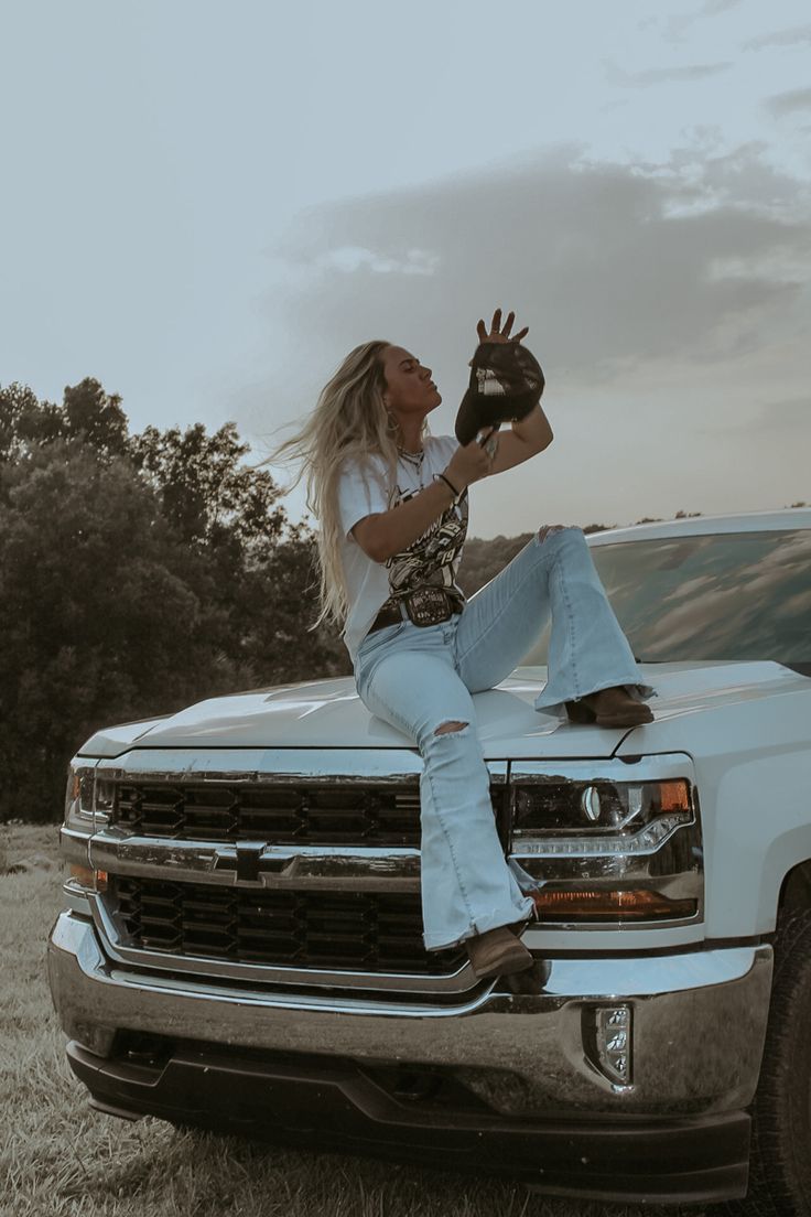 a woman sitting on the hood of a white truck with her hand up in the air