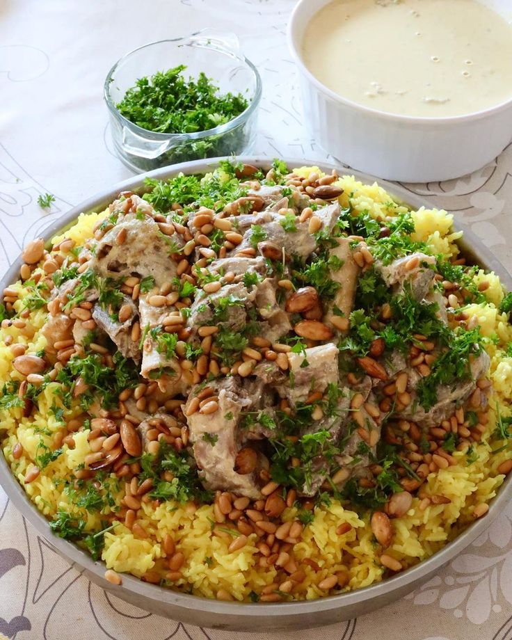 a large bowl filled with rice and meat covered in herbs next to a cup of soup