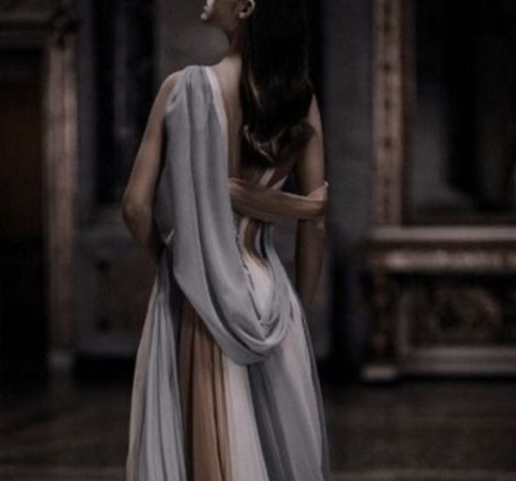 a woman with long hair wearing a gray and beige dress standing in an empty room