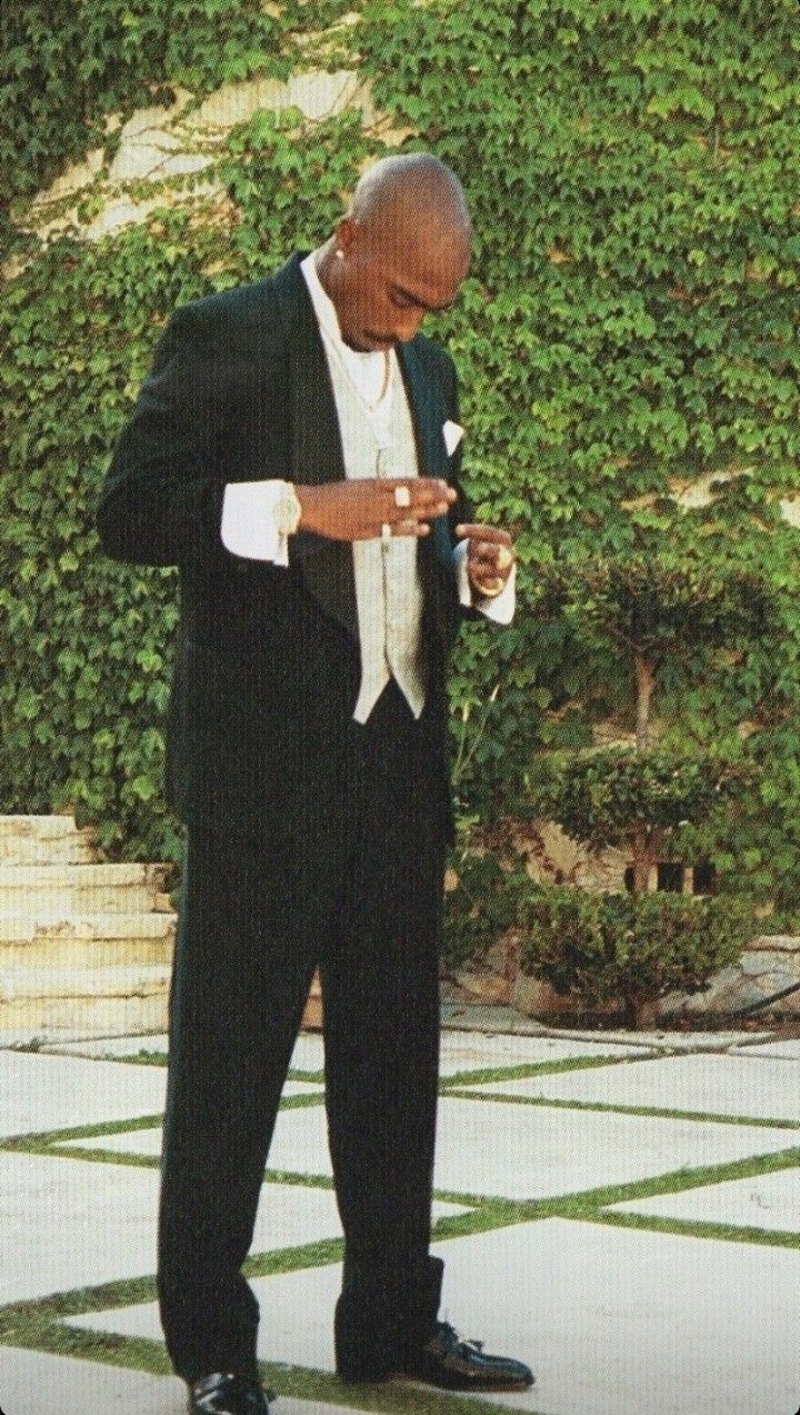 a man in a tuxedo looking down at his cell phone while standing outside