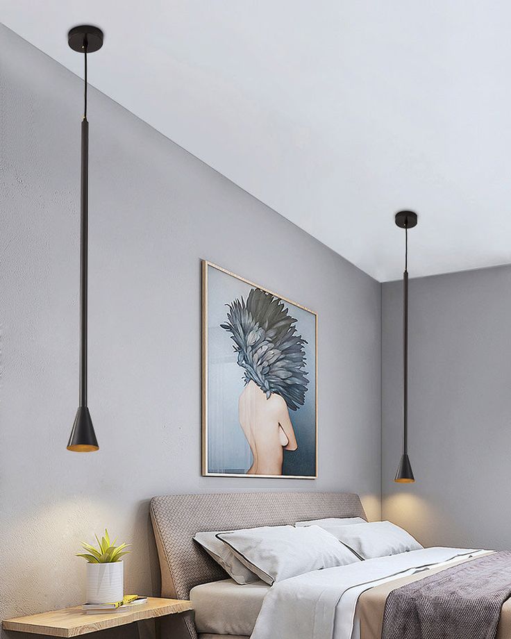 a bed sitting under two hanging lights next to a table with a plant on it