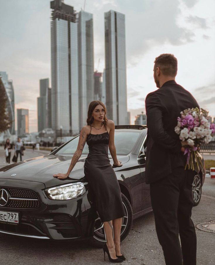 a woman standing next to a man in front of a black car with flowers on it