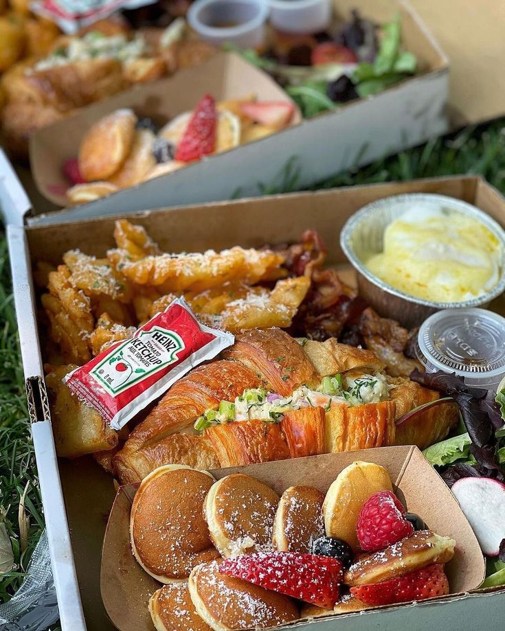 an open box filled with pastries and desserts next to other food on the ground