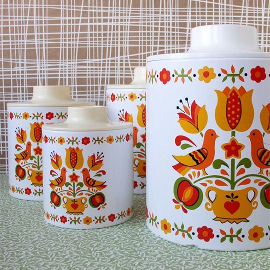 three canisters with colorful designs on them sitting on a table next to a wall