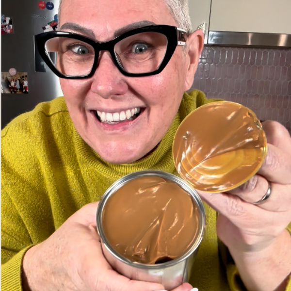 an older woman with glasses holding a jar of chocolate in front of her face and smiling at the camera