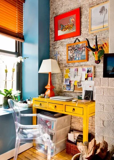 a yellow desk in front of a window with pictures on the wall and a lamp next to it