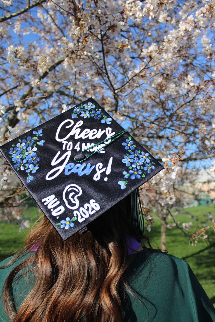 Girl with brown hair wearing a graduation cap titled “Cheers to 4 more Years” with an ear and blue flowers. Gods Favor, Yearbook Quotes, Grad Caps, Ohio University, Grad Photos, Grad Cap, College Graduation, Graduation Cap, Crafts To Do