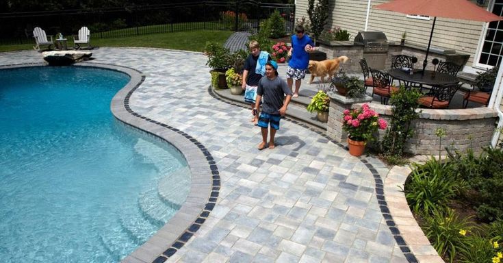 several people are walking around the backyard with a pool in the foreground and a dog on the other side