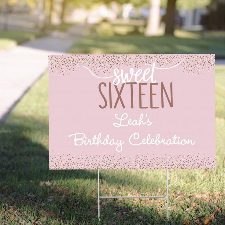 a pink sign sitting on top of a grass covered field next to a sidewalk and trees