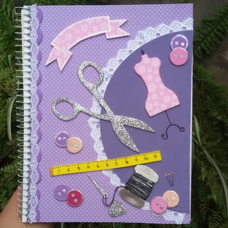 a hand holding a purple notebook with sewing and buttons on it, along with a measuring tape