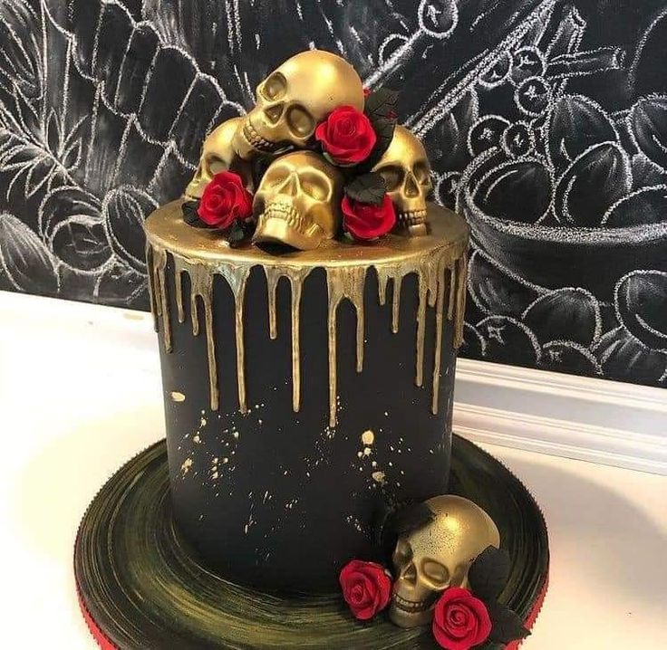 a black cake with gold icing and red roses on the top is decorated with skulls