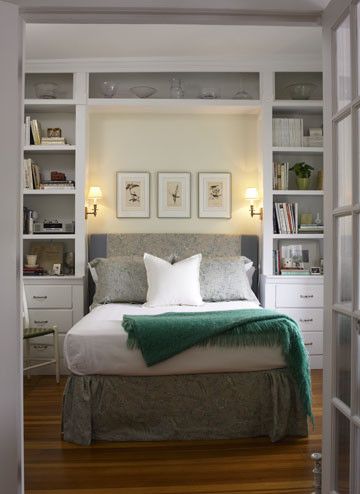 a bed sitting inside of a bedroom next to a white book shelf filled with books